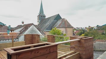 A wooden deck with a metal railing, overlooking a town with buildings and a church steeple.