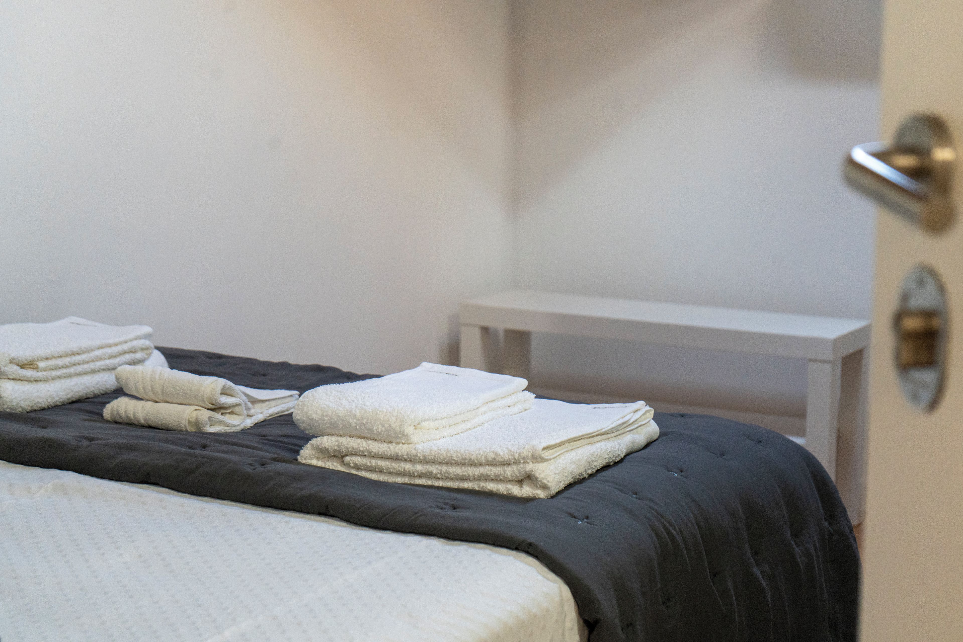 A neatly made bed with a dark-colored bedspread and white towels folded on top.