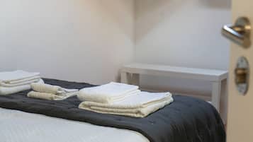 A neatly made bed with a dark-colored bedspread and white towels folded on top.
