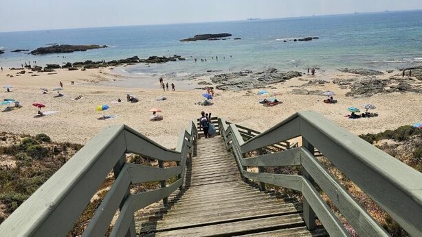 Una scala di legno che conduce a una spiaggia con ombrelloni e persone.