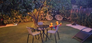 An outdoor patio with a round table and chairs, surrounded by lush greenery and a wooden fence.
