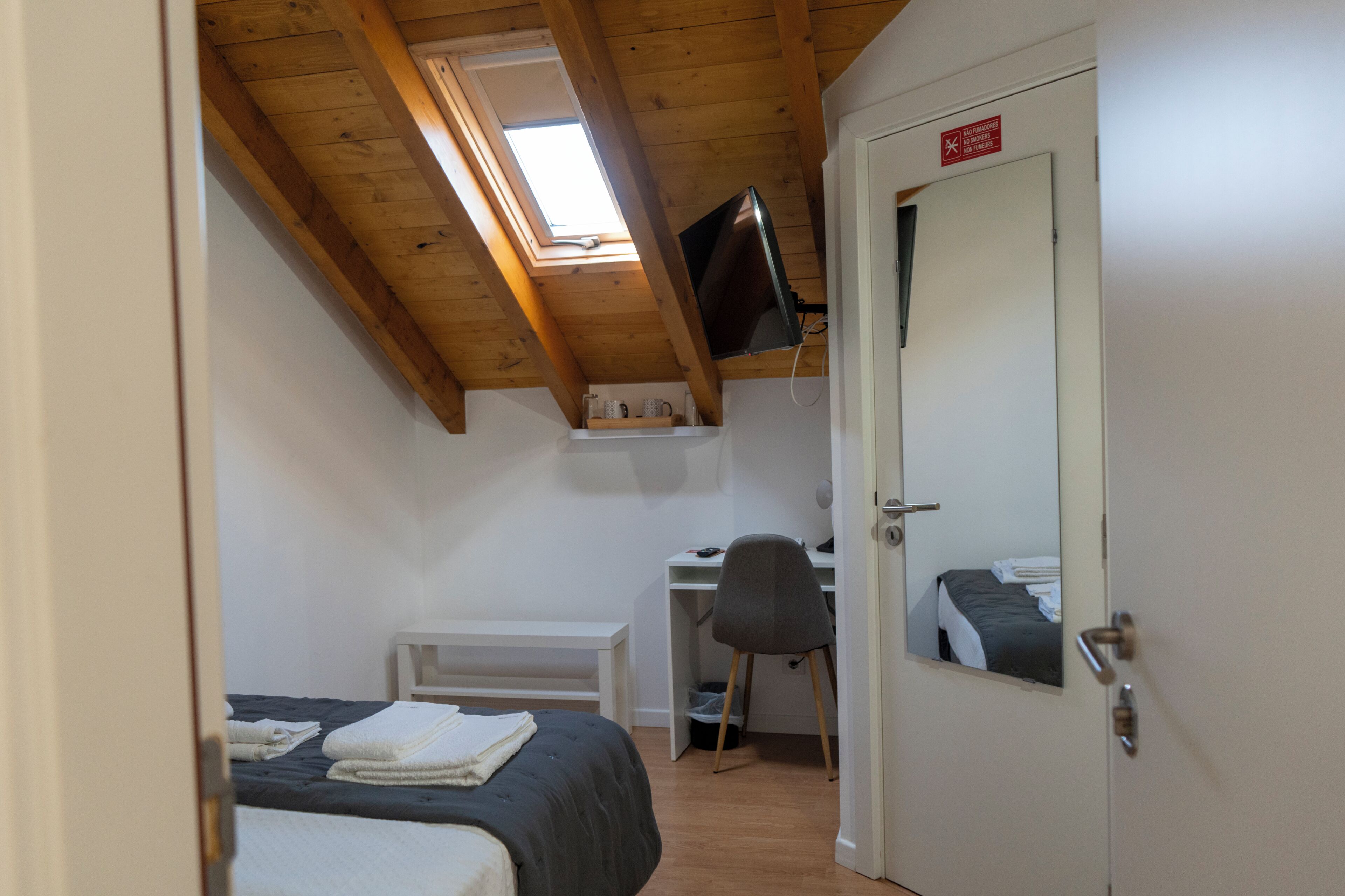 A bedroom with a bed, a desk, a chair, a television, and a door with a sign.