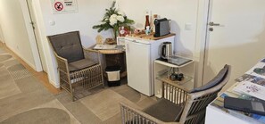 Una kitchenette compacta con refrigerador, cafetera y una pequeña mesa con una silla.