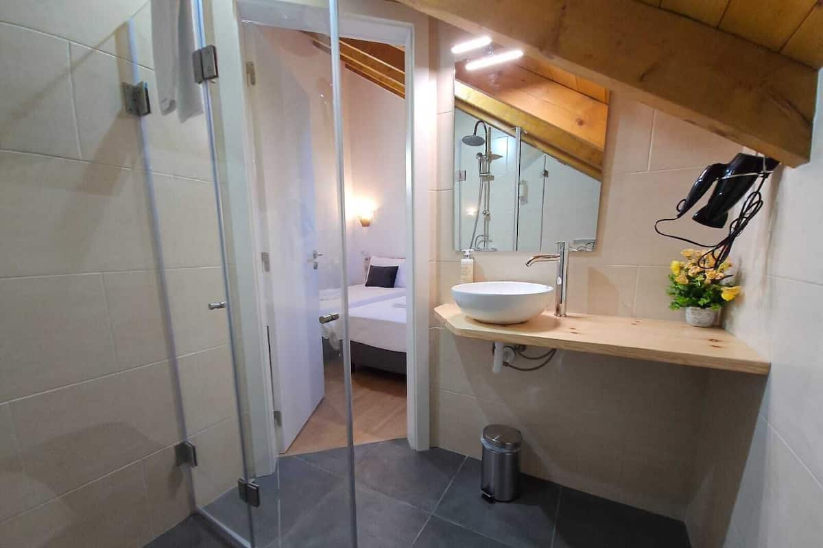 Un baño moderno con mampara de vidrio, lavamanos blanco y un pequeño cubo de basura.