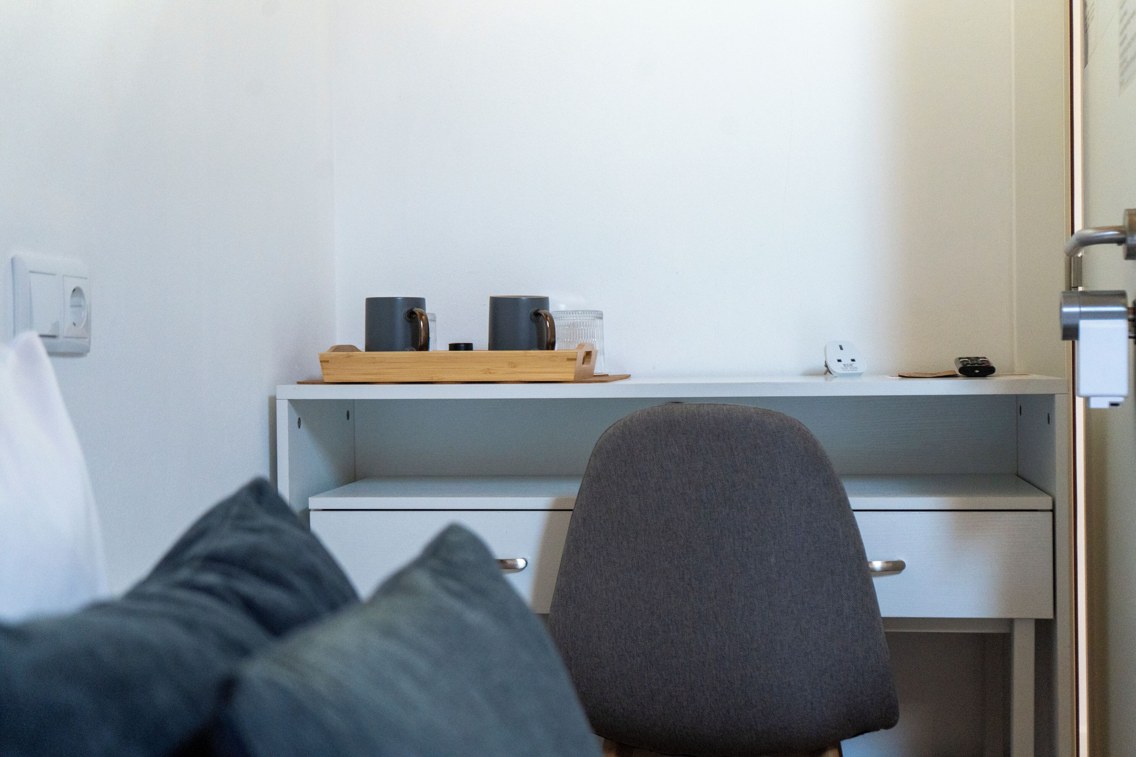 Una habitación con una cama, un escritorio con una bandeja de objetos y una silla.