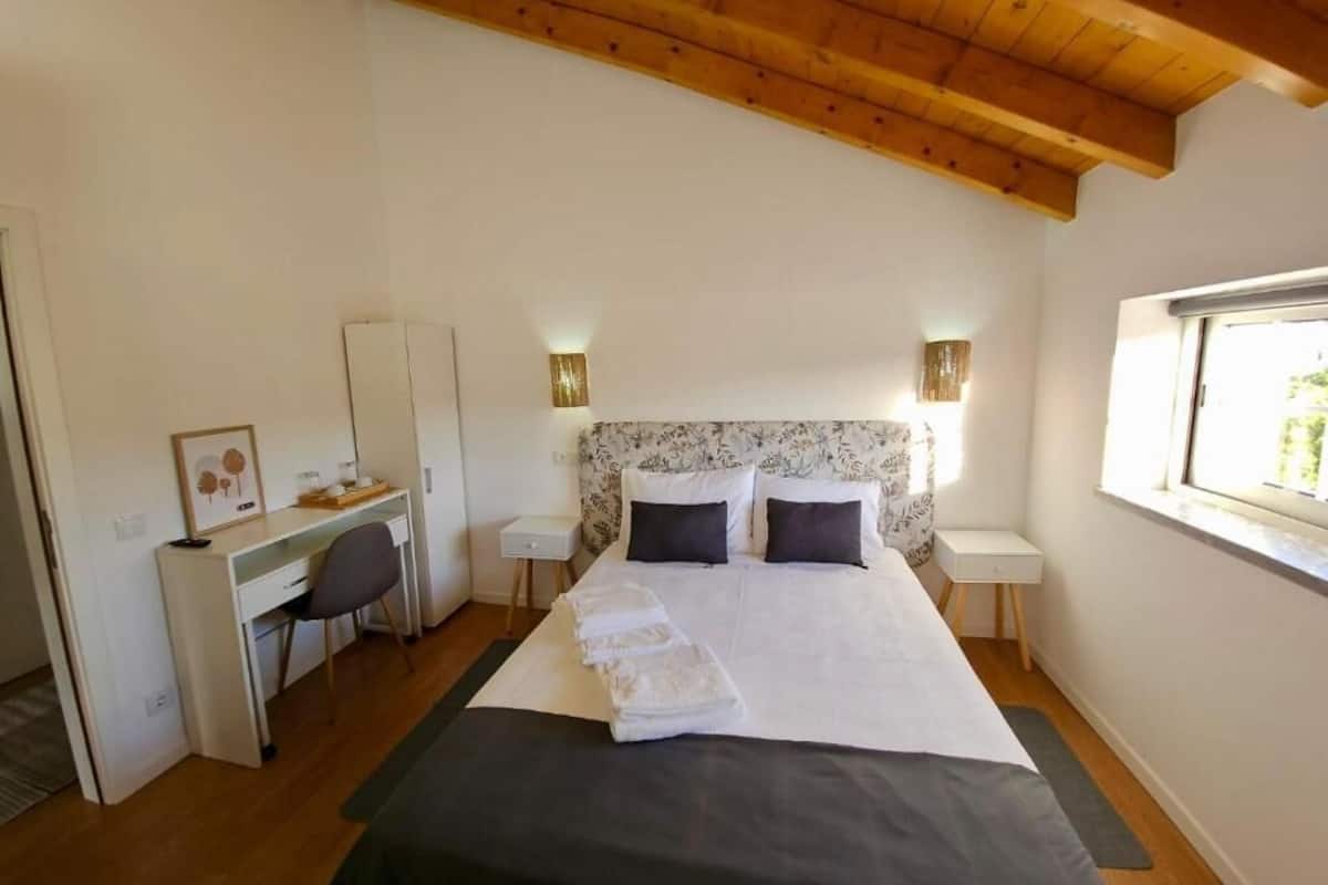 Une chambre à coucher comprenant un lit, un bureau, une chaise, des tables de chevet et une fenêtre.