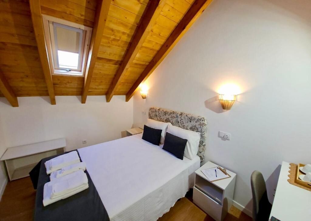 Un dormitorio con techo de madera, una cama con ropa blanca, una mesita de noche, un escritorio y una silla.