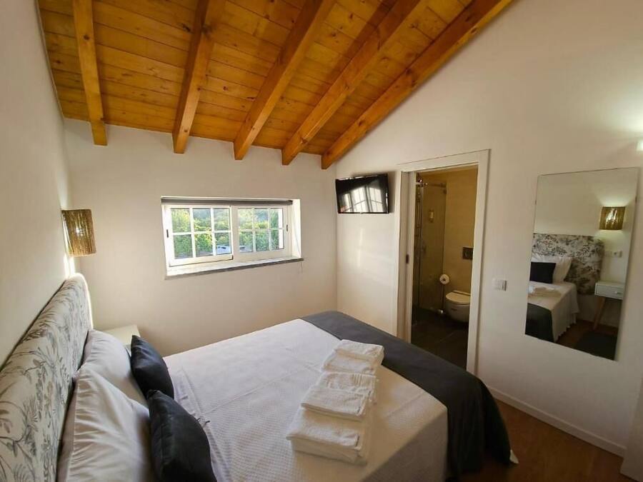 Ein Schlafzimmer mit Holzboden, einem Bett mit weißer Bettwäsche, einem Fenster, einer Tür zu einem Badezimmer und einem Spiegel an der Wand.