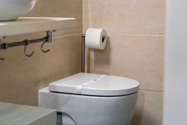 Inodoro blanco con dispensador de toallas de papel montado en la pared junto a él.