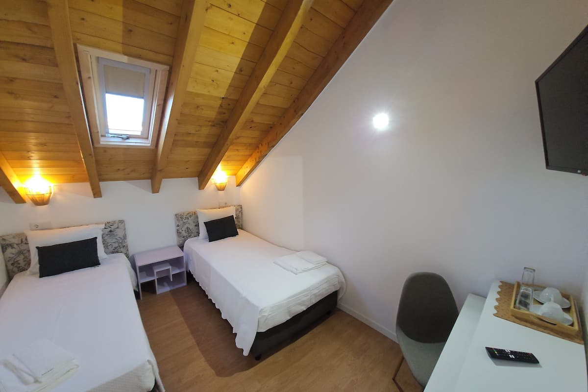 A room with two beds, a desk, a chair, a window, and a ceiling light.