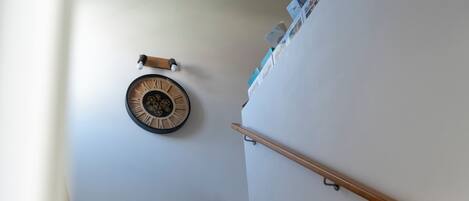 A wooden staircase with a handrail, a wall-mounted clock, and a small shelf with items.
