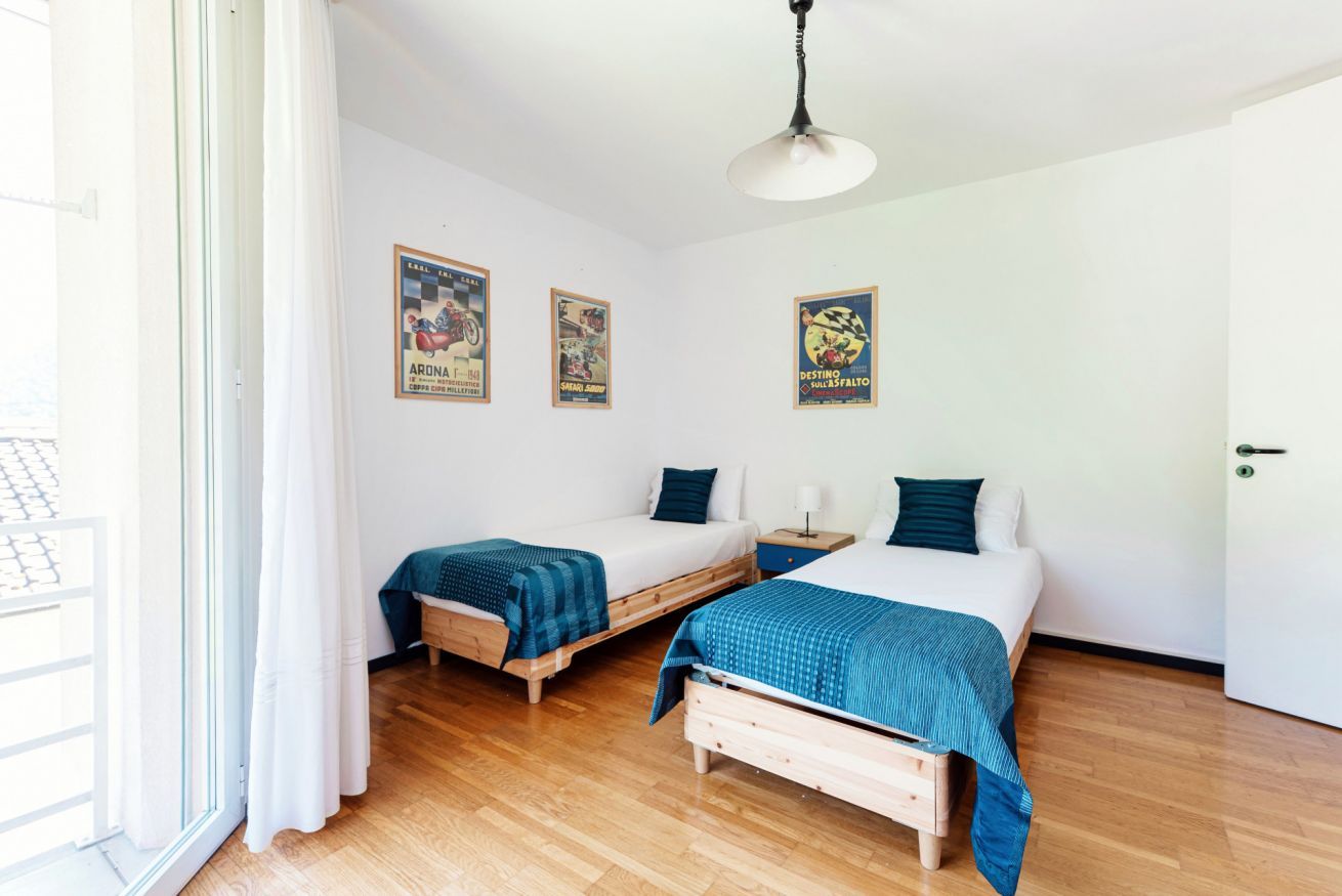 A room with two single beds, a wooden floor, a white ceiling, and a door.