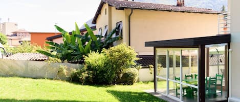 Una propiedad residencial con jardín, un patio con sillas verdes y vistas a la montaña.