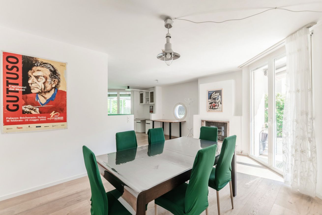 A dining area with a table and chairs, a poster on the wall, and a view through a glass door.