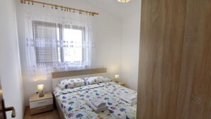 Un dormitorio con una cama, mesitas de noche, una ventana con cortinas de encaje y una puerta de madera.