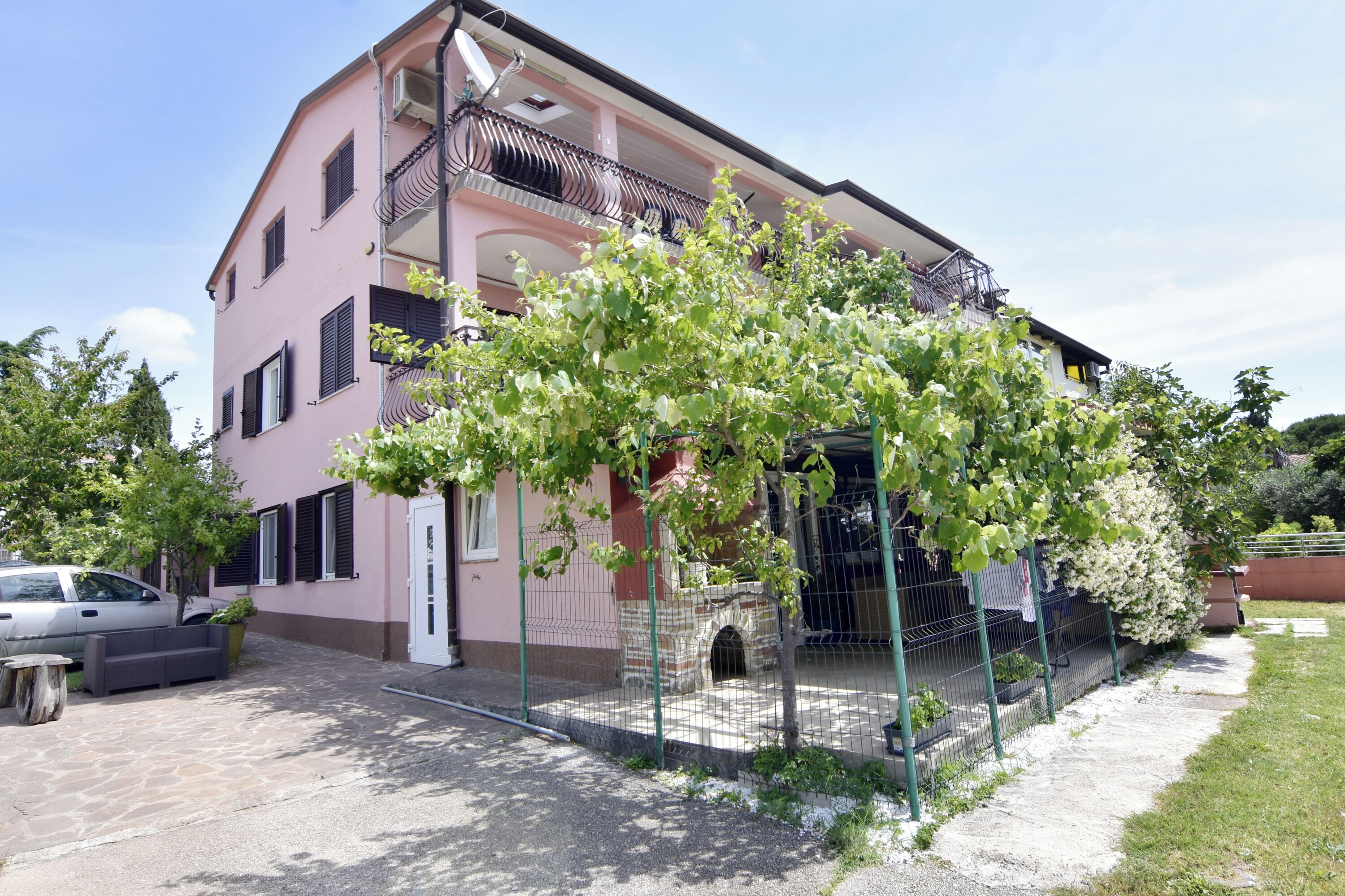 Un bâtiment rose avec un banc en pierre, une voiture et un jardin clos.
