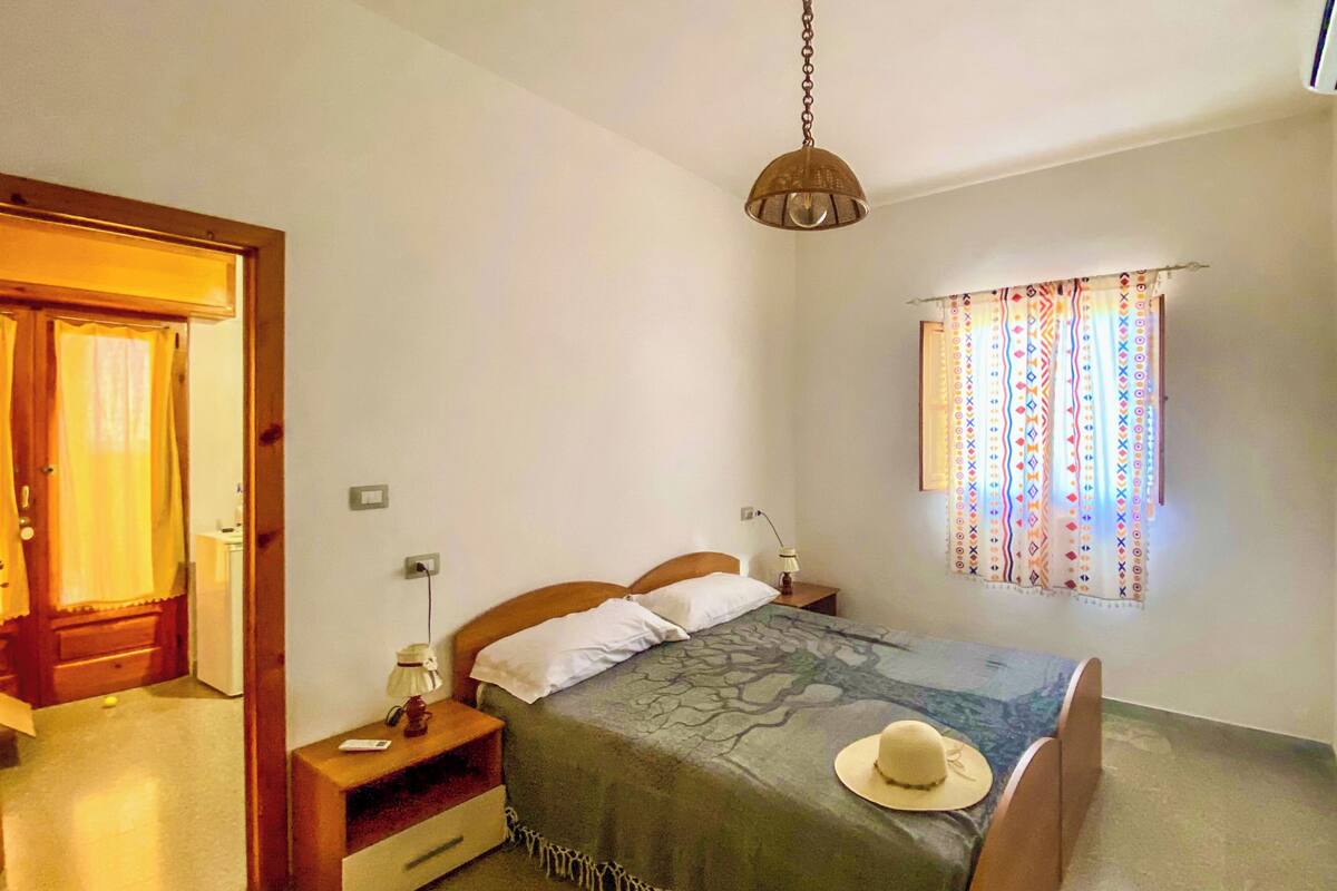 A bedroom with a bed, bedside table, lamp, and a window with curtains.