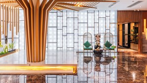 A modern lobby with a wooden reception desk, a seating area with green cushions, and a patterned wall. - Immersing Hotel (Chengdu)