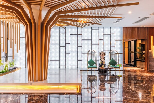 A modern lobby with a wooden reception desk, a seating area with green cushions, and a patterned wall.