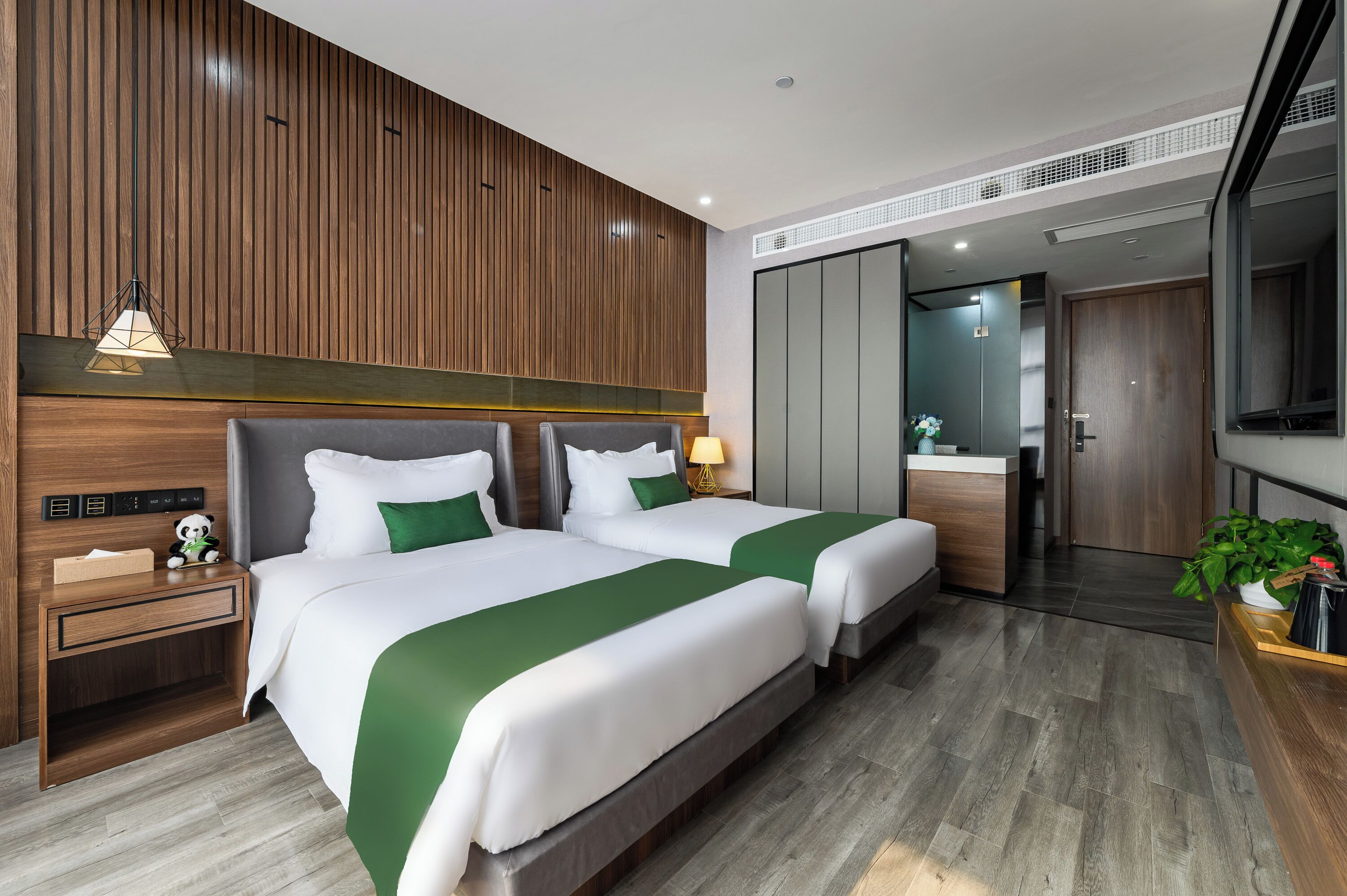 Habitación de hotel con dos camas, un panel de madera en la pared, una mesita de noche con lámpara y vistas al baño.