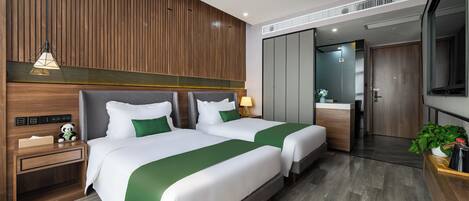 Habitación de hotel con dos camas, un panel de madera en la pared, una mesita de noche con lámpara y vistas al baño.