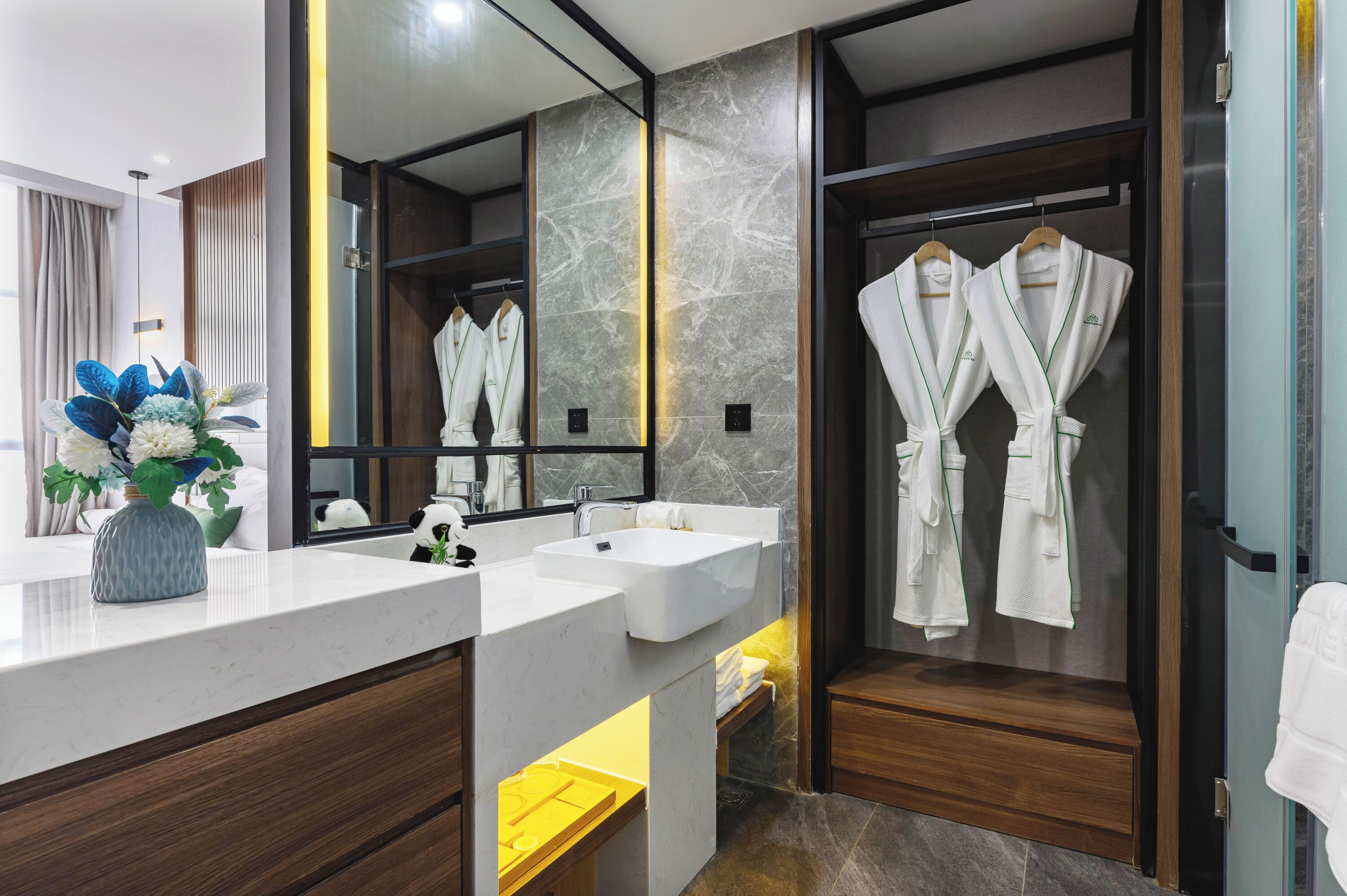 A modern bathroom with marble walls, dual sinks, a large mirror, and wooden cabinets.