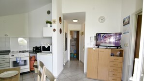 Eine kompakte Küche mit Herd, Backofen und Mikrowelle, ein Essbereich mit Stühlen und Tisch sowie ein Fernseher auf einer Holzkommode.