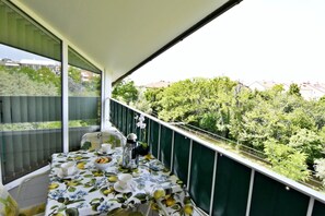 A balcony with a table set for two, overlooking a lush green area with trees and buildings in the background. - Prime location apartment nicely equipped (Zambratija)
