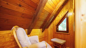 Ein Holzhütten-Interieur mit einem einzelnen Holzstuhl und einer Bank, einem Fenster und einer schrägen Decke.