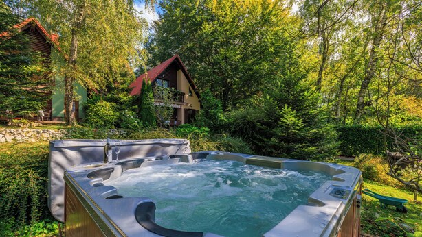 Ein Whirlpool in einem üppigen Garten mit einer Holzhütte im Hintergrund.