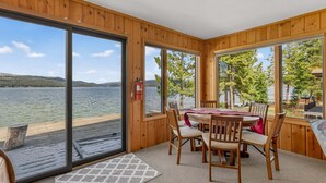Une cabane en bois avec une table et des chaises, de grandes fenêtres donnant sur un lac, et un extincteur fixé au mur.
