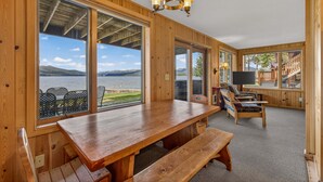 Une cabane en bois dotée de grandes fenêtres, d’une table en bois et d’un banc.