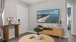 A living room with a round coffee table, a TV mounted on the wall, a wooden console table, and a door.