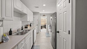 A narrow kitchen with white cabinets, a stainless steel sink, and a refrigerator.
