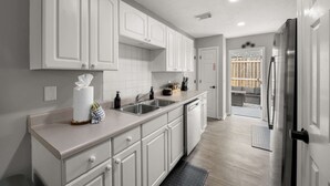 A kitchen with white cabinets, a countertop, a sink, and a refrigerator.