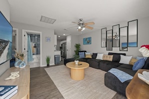 A modern living room with a dark-colored sofa, a round wooden coffee table, and a ceiling fan.