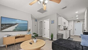 A modern living room with a large TV, a round wooden coffee table, a dark grey sofa, and a ceiling fan.