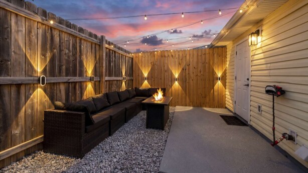 A covered outdoor patio with a wooden fence, a fire pit, and string lights.