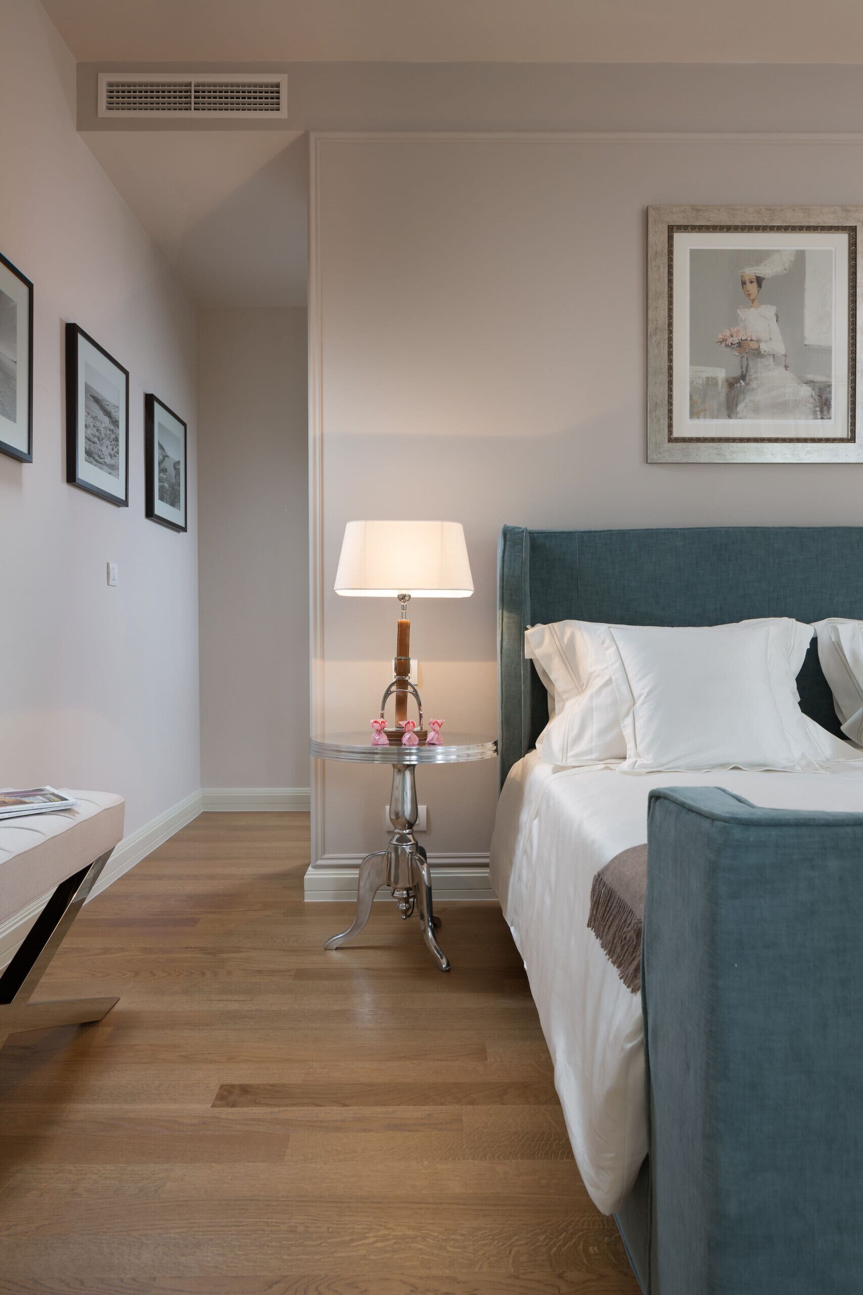 Une chambre d’hôtel avec un lit, une table de chevet avec une lampe, un tableau encadré au mur et un plancher en bois.