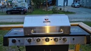 Een Char-Broil gasgrill met vier branders, een bijkomende brander en een waterlade, geplaatst op een houten terras.