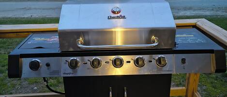 Een Char-Broil gasgrill met vier branders, een bijkomende brander en een waterlade, geplaatst op een houten terras.