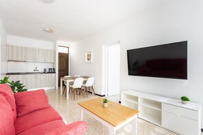 A modern living room with a red sofa, a wooden coffee table, a TV mounted on the wall, and a kitchen in the background. - Las Américas lovely pool view (Arona)