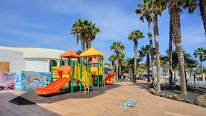 Ein Spielplatz mit Rutschen und Klettergerüsten, umgeben von Palmen und blauem Himmel.
