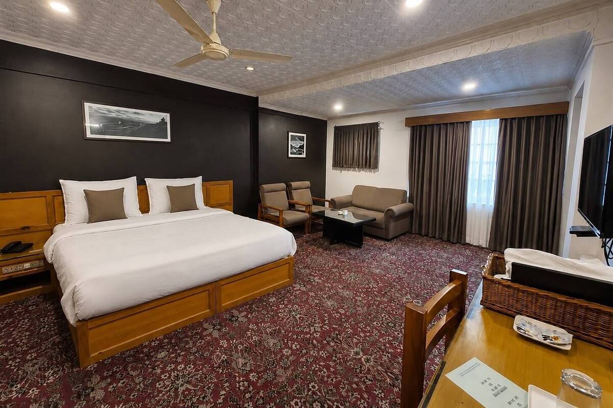 Habitación de hotel con cama, escritorio, sillón, sofá, televisor y ventilador de techo.