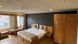 A bedroom with a large bed, a desk, a chair, a wardrobe, and a window. - Hotel Meridien River Front Rajbagh (Srinagar)