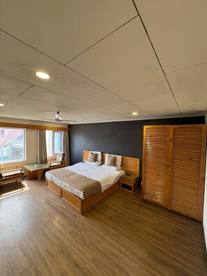 A bedroom with a large bed, a desk, a chair, a wardrobe, and a window. - Hotel Meridien River Front Rajbagh (Srinagar)