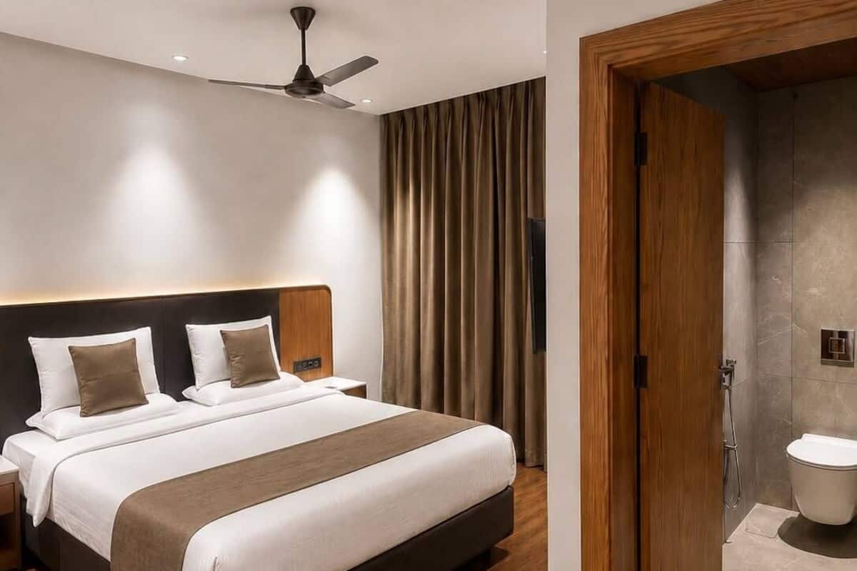 Una habitación de hotel moderna con una cama grande, un ventilador de techo, un baño con inodoro y ducha, y suelo de madera.