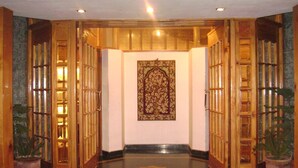 A hallway with wooden doors, a patterned wall hanging, and potted plants. - Hotel Meridien River Front Rajbagh (Srinagar)