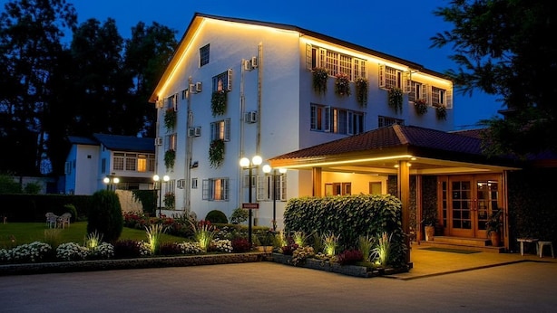 A multi-story hotel with a covered entrance, outdoor lighting, and a well-maintained garden. - Hotel Meridien River Front Rajbagh (Srinagar)