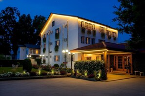 A multi-story hotel with a covered entrance, outdoor lighting, and a well-maintained garden. - Hotel Meridien River Front Rajbagh (Srinagar)